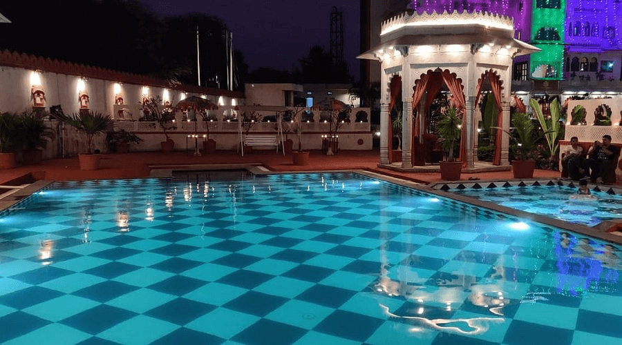 Night pool deck with warm ambient candlelight, seating gazebos, and starlit sky