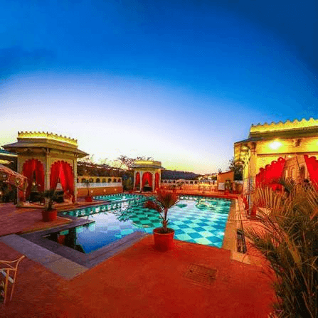 Twilight sky over illuminated poolside courtyard with red drapes and palm foliage